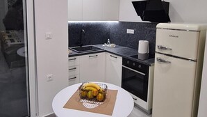 Une cuisine moderne avec des meubles blancs, un plan de travail noir, un réfrigérateur blanc et une table à manger agrémentée d’un panier de fruits.
