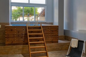 Ein Badezimmer mit einer Holzbank, einer Holzeiter und einem Fenster mit Blick auf Bäume und ein Gebäude.