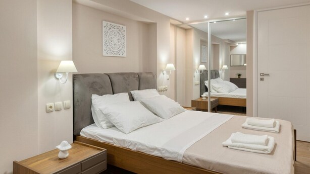 Ein modernes Hotelzimmer mit einem großen Bett, Nachttischlampen, einem Spiegel und einem Nachttisch mit Lampe.
