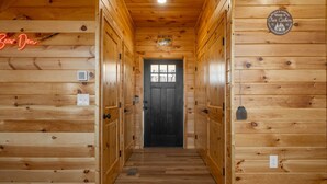 A wooden cabin interior with a black door, wooden walls, and a neon sign. - Brand New Luxury Cabin On 2.7 Acres | Fire Pit (Berkeley Springs)