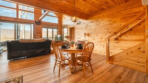A wooden cabin interior with a dining area, a sofa, and a staircase. - Brand New Luxury Cabin On 2.7 Acres | Fire Pit (Berkeley Springs)