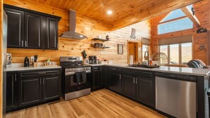 A modern kitchen with wooden walls, black cabinets, stainless steel appliances, and a large window. - Brand New Luxury Cabin On 2.7 Acres | Fire Pit (Berkeley Springs)