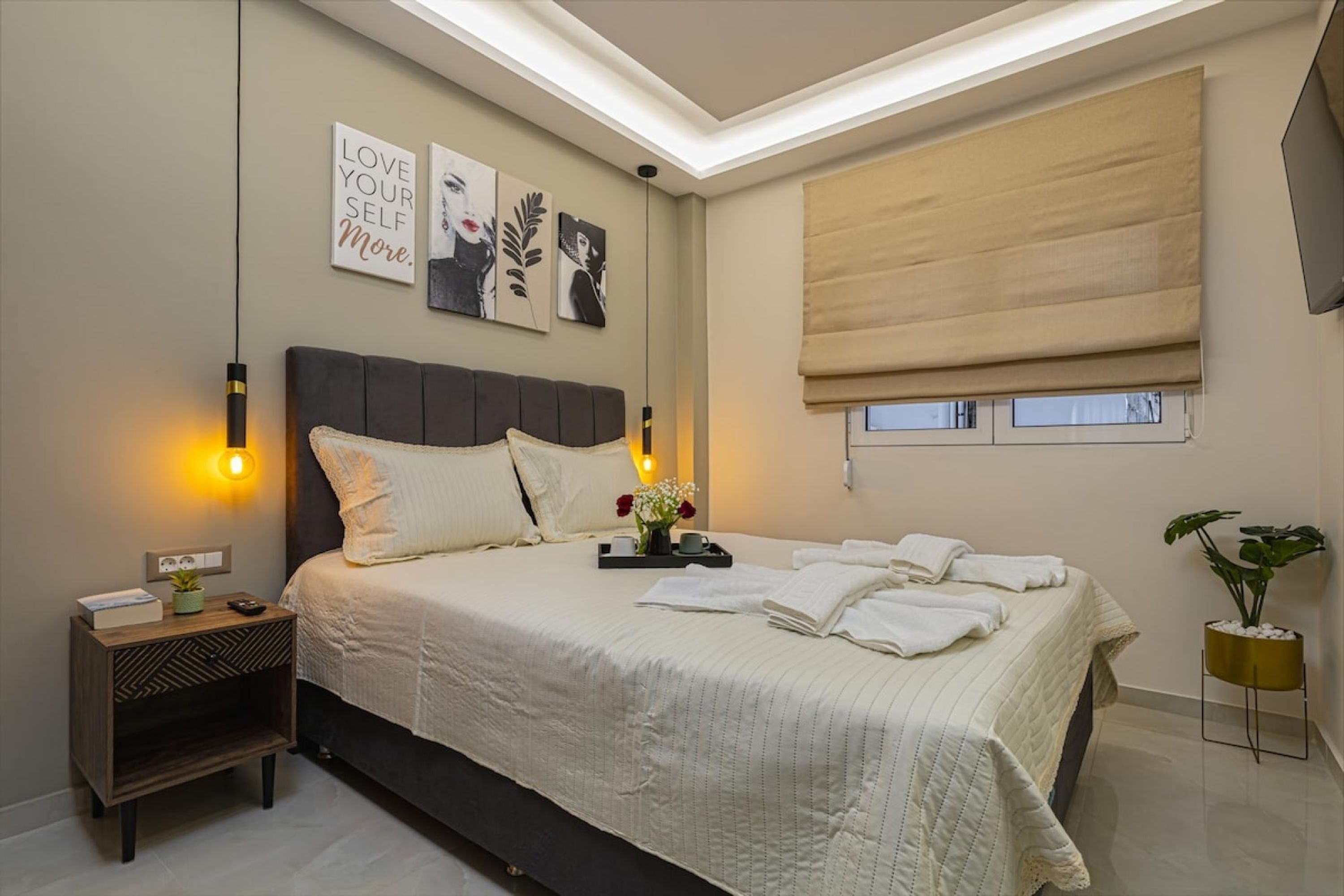 Una camera da letto con un letto grande, comodini, un tavolino, una TV a parete e una finestra con tenda.