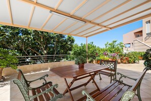 An outdoor patio with a wooden table and benches, surrounded by potted plants and a clear sky. - Sofie's Garden View Apartment (Daratsos)