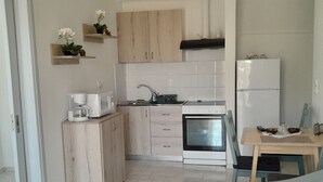 A modern kitchen with wooden cabinets, a built-in oven, and a dining area with a table and chairs. - Sun & Beach Apartments in Chania 11 (Chania)