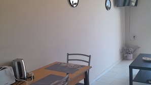Een eetgedeelte met een tafel, stoelen, een waterkoker en een broodrooster. Er zijn wandspiegels en een flatscreen televisie.