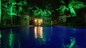 A nighttime view of a pool area with a stone building, palm trees, and a staircase leading to a door. - Chalé De Canoa (Aracati)