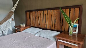 A bed with a wooden headboard, two bedside tables, a nightstand, a hammock, and a potted plant. - Chalé De Canoa (Aracati)