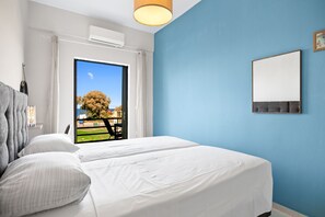 Ein Hotelzimmer mit einem großen Bett, Blick auf einen Baum und einen Park durch eine Schiebetür, und einer blauen Wand.