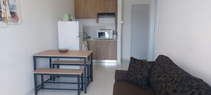 Eine kleine Küche mit Kühlschrank, Mikrowelle und Toaster. Es gibt einen Esstisch mit Bänken und eine Couch mit floralen Kissen.