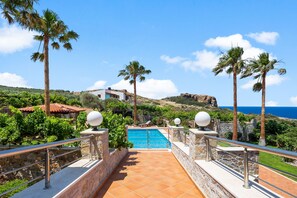 A pool area with stone railings, palm trees, and a view of the sea. - Kambos Horizon Villa (Kampos)