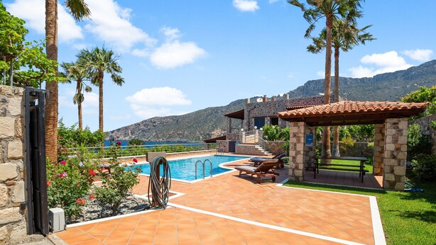 A pool area with a stone patio, lounge chairs, and a pergola. - Kambos Horizon Villa (Kampos)