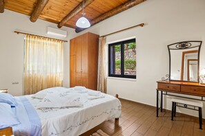 Ein Schlafzimmer mit einem Bett, einem Holzschrank, einem Schreibtisch mit Spiegel und einem Fenster mit Blick auf Grünflächen.