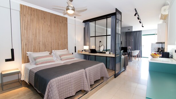 Een moderne slaapkamer met een groot bed, nachtkastjes, een bureau en uitzicht op de keuken.