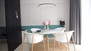 Een eethoek met een ronde tafel, witte stoelen, een vaas met bloemen en een moderne hanglamp.