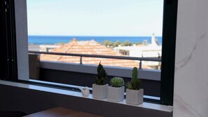 Un rebord de fenêtre orné de quatre plantes en pot, avec vue sur la mer et les bâtiments.