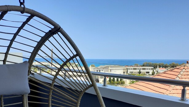 Une chaise en osier avec des coussins, placée sur un balcon donnant sur une vue panoramique de la côte.
