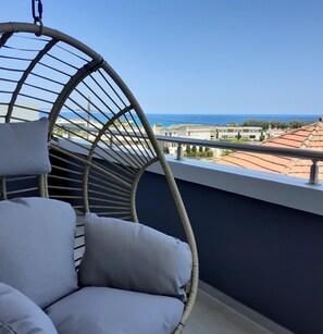 Une chaise en osier avec des coussins, placée sur un balcon donnant sur une vue panoramique de la côte.