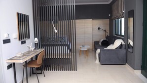 Un salon moderne comprenant un canapé, une table à manger avec des chaises, une petite table ronde avec une lampe, et une grande fenêtre avec des rideaux.