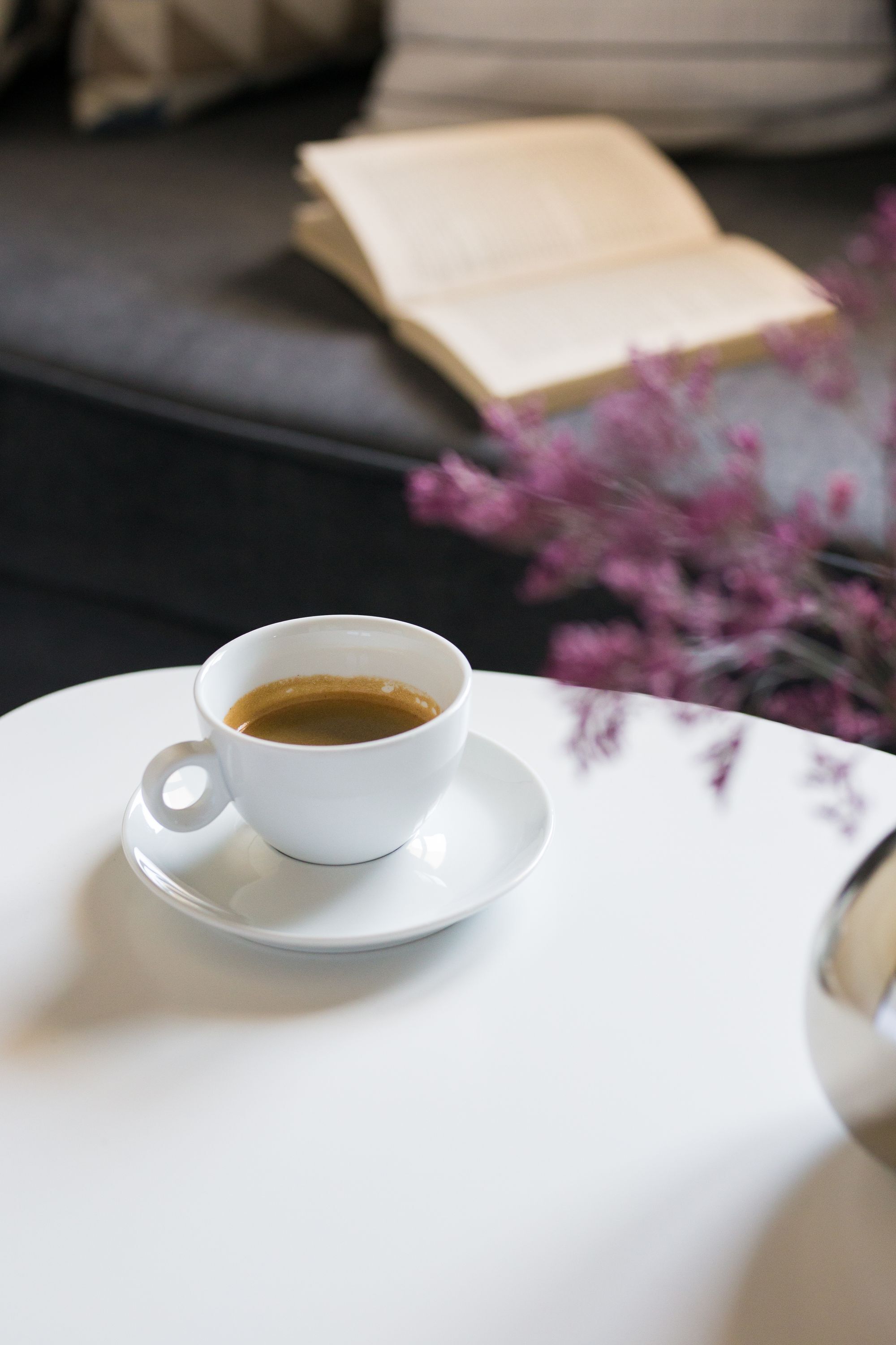 Una taza de café blanca sobre un plato pequeño blanco, sobre una mesa blanca.