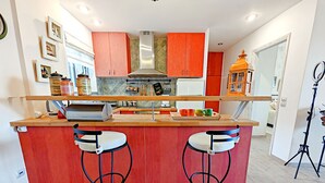 Une cuisine moderne dotée d’un îlot central, de deux tabourets de bar et de meubles de rangement rouges.