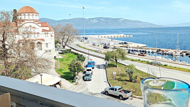 Une vue depuis un balcon donnant sur une route côtière, avec une église, des voitures garées et un ciel dégagé.