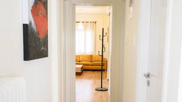 A hallway with a wooden floor, a coat rack, a yellow sofa, and a painting on the wall.