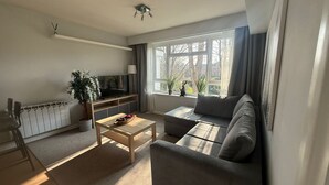 A modern living room with a sofa, a coffee table, a TV, and a radiator. - Central Horsham Flat | Free Parking (Horsham)