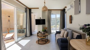 A modern living room with a sofa, a round wooden table, a TV, and a view of the outdoors. - Gaea Dream Villas Complex (Tinos ,Loutra)