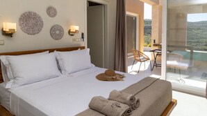 A hotel room with a bed, decorative wall art, a hat, towels, and a balcony with a view. - Gaea Dream Villas Complex (Tinos ,Loutra)