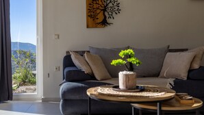 Ett modernt vardagsrum med en mörkblå soffa, ett runt soffbord med ett bonsaiträd och ett konstverk i trä som hänger på väggen.