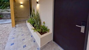 A building entrance with a dark door marked with the number 28, a tiled pathway, and a planter box with plants. - Hotel Avila (Valladolid)