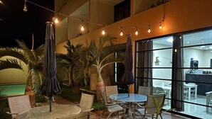 An outdoor patio area with round tables and chairs, string lights, and umbrellas. - Hotel Avila (Valladolid)