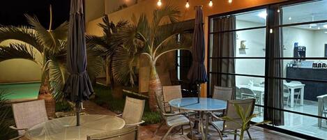 An outdoor patio area with round tables and chairs, string lights, and umbrellas.