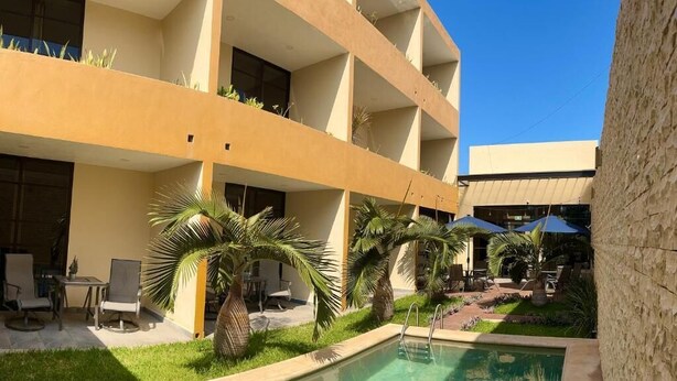 A hotel courtyard with a swimming pool, outdoor seating, and palm trees. - Hotel Avila (Valladolid)