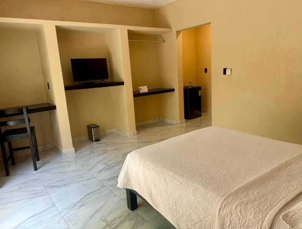 A hotel room with a bed, a desk with a television, a chair, and a trash bin.