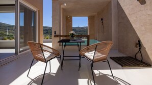 A balcony with a table and two wicker chairs, overlooking a pool and a mountainous landscape. - The Pyr Element Of Gaea (Loutra)