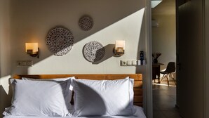 A neatly made bed with white linens, a wooden headboard, and decorative wall sconces with lighted candles. - The Pyr Element Of Gaea (Loutra)