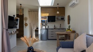 A modern living room with a sofa, a TV, and a dining area with a table and chairs. - The Pyr Element Of Gaea (Loutra)