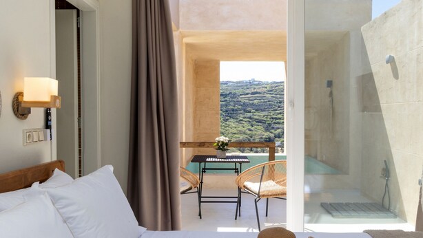 A hotel room with a bed, a dining table with chairs, and a view of the landscape. - The Pyr Element Of Gaea (Loutra)
