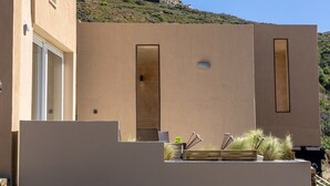 Ein modernes Gebäude mit minimalistischem Design, das ein Flachdach und große Fenster aufweist. Im Hintergrund ist ein felsiger Hügel zu sehen.