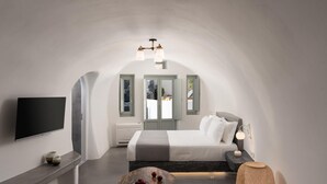 Een moderne slaapkamer met een gebogen plafond, een bed met witte lakens, een flatscreen televisie en een klein tafeltje met fruit.