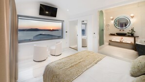 Een moderne slaapkamer met een groot raam, een bed, nachtkastje, televisie, en een badkamer met spiegel en planken.