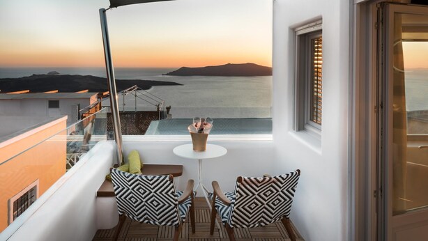 Een balkon met een tafel en stoelen, met uitzicht op de kust bij zonsondergang.