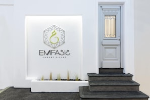 A white wall with a logo and text for "EMFASIC LUXURY VILLAS". - Emfasis Luxury Villa (Fira)