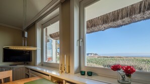 A kitchen with a TV, a dining table, and a window with a view of the countryside. - Apartment Watt directly on the mudflats in Rantum on Sylt (Sylt)