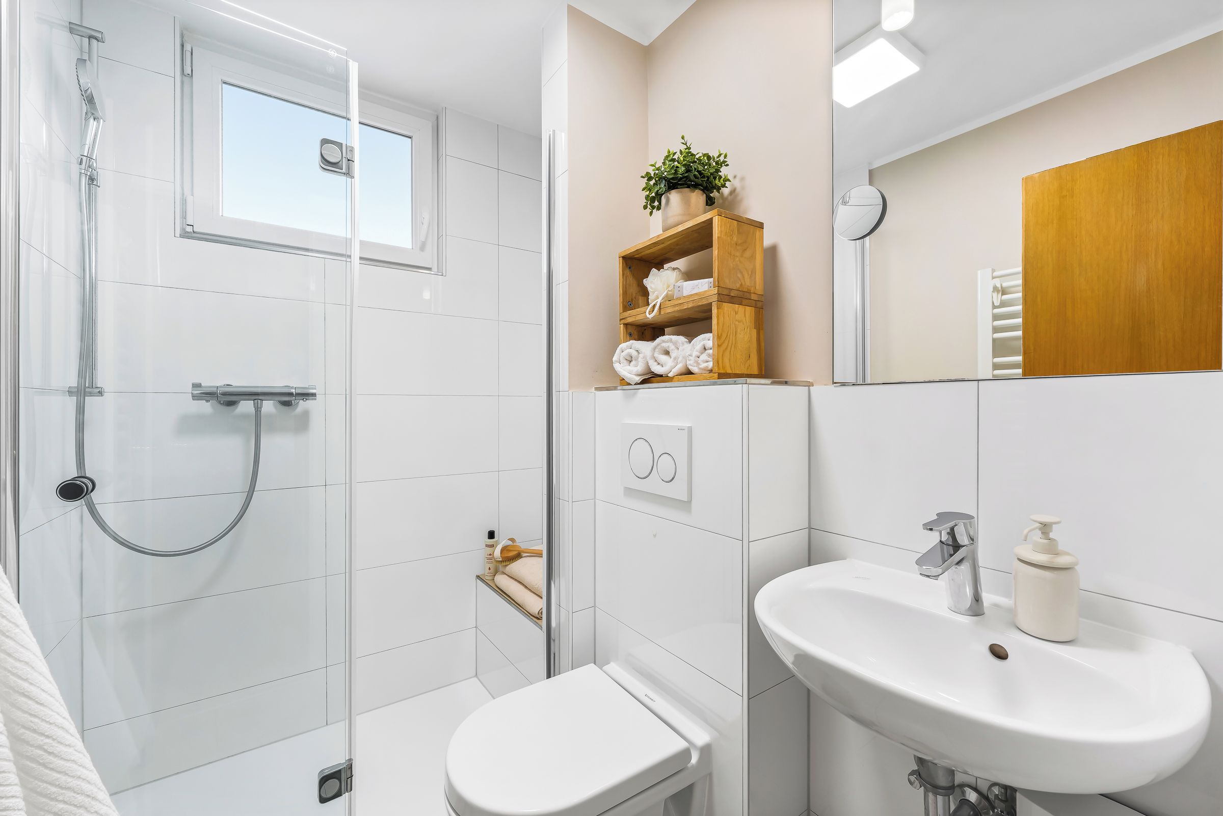 Ein modernes Badezimmer mit Glasdusche, Toilette, Waschbecken und einem Holzboden mit Handtüchern.