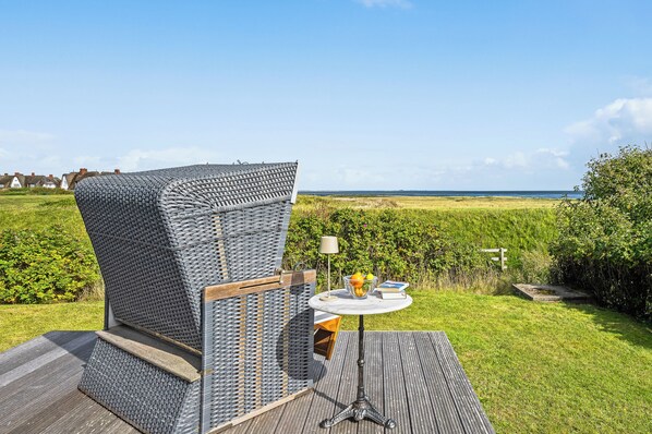 A wicker chair with a view of the sea, a round table with a lamp, and a book. - Watt Apartment, right on Rantum Bay on Sylt (Sylt)