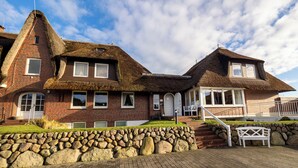 A traditional brick house with thatched roofs, a stone wall, and a wooden deck with a bench. - Apartment Watt directly on the mudflats in Rantum on Sylt (Sylt)