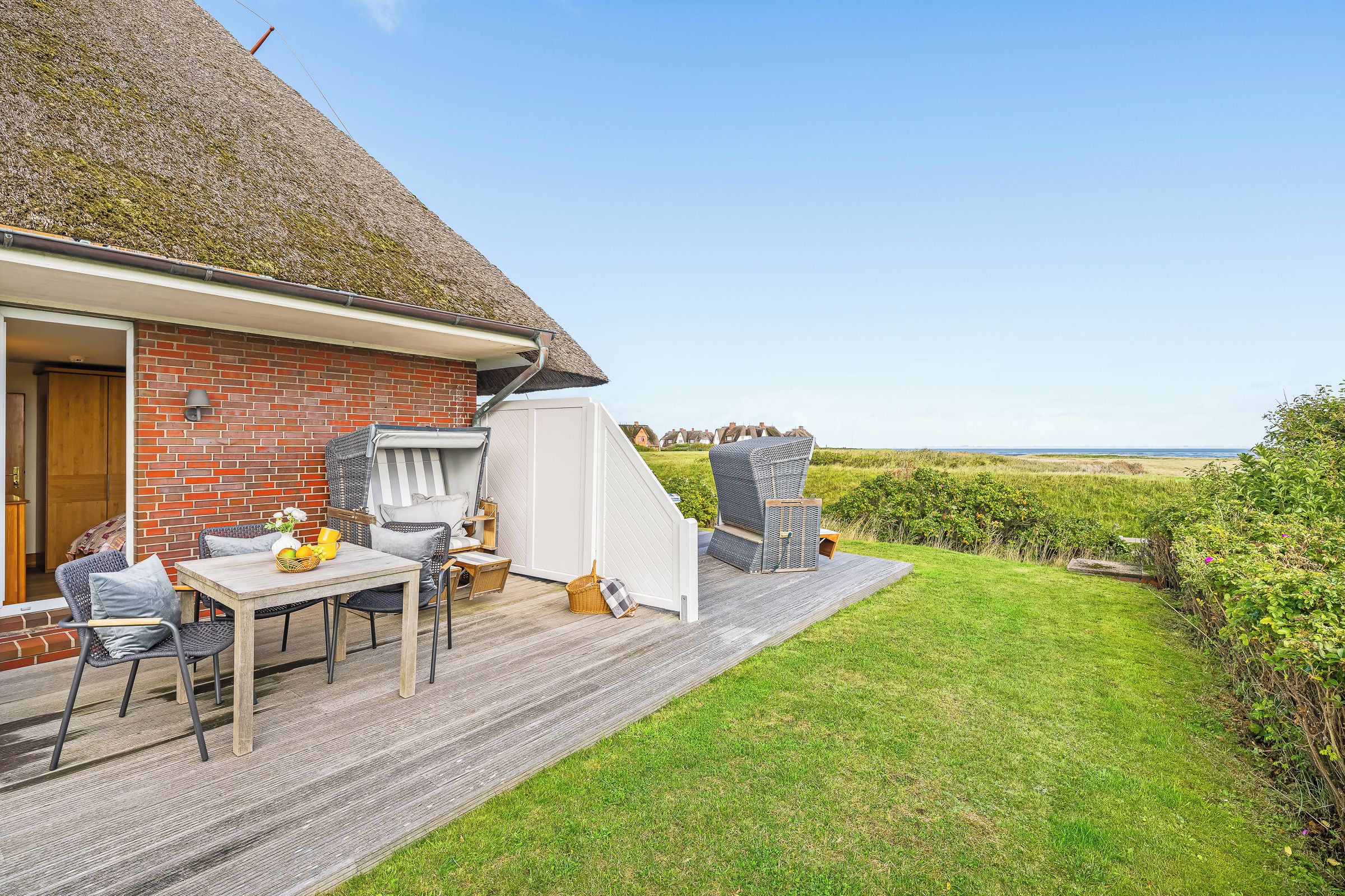 Ein Haus mit Backsteinfassade, einem Reetdach, einer Holterrasse und Blick aufs Meer.
